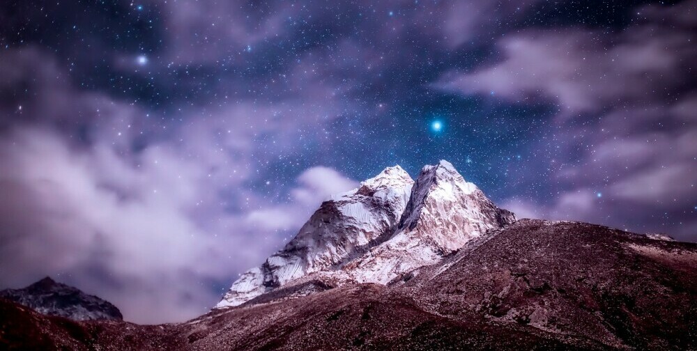 One bright star mid many stars, shining over steep snow-covered mountain