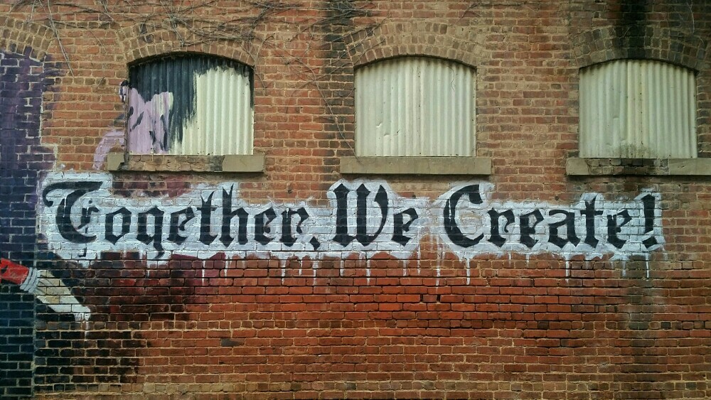 Together, We Create! A sign spray painted onto a brick building